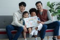 Happy Asian young LGBTQ gay couple with little cute adopted Caucasian and African kid smiling and showing rainbow family drawing Royalty Free Stock Photo
