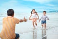 Happy asian young single dad playing with his children boy and girl, they running on sandy beach during sunny day with laughing