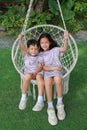 Happy Asian young sister and little brother sitting together on the white cradle in the garden. Boy and girl play swing Royalty Free Stock Photo