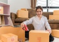 Happy Asian young woman is online small business ecommerce owner packing and taping into carton boxes moving delivery to customer