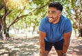 Happy athletic mixed race man smiling while standing with his hands on his knees in a park. Hispanic male resting after