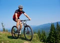 Happy athletic tourist cyclist in helmet, sunglasses and full equipment riding bike on grassy hill Royalty Free Stock Photo