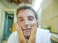 Happy and attractive Caucasian man smiling fresh at home bathroom washing his face with exfoliant soap looking at himself in toile Royalty Free Stock Photo