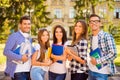 Happy attractive diverse five students standing near university and holding notebook