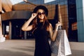 Happy attractive elegant girl, in a black dress and hat, wearing dark glasses, holding shopping bags and enjoying shopping. Black Royalty Free Stock Photo