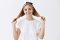 Happy attractive and emotive blond woman in headband and white t-shirt pulling hair strands with hands and smiling