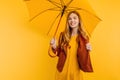 Happy girl, in a bright yellow dress and autumn jacket, stands with a yellow umbrella on an  yellow background. concept of Royalty Free Stock Photo