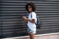 Happy attractive girl in the city street using mobile phone, checking social media and emails. Woman with afro hairstyle in