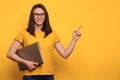 Happy attractive girl holding computer and pointing with finger at blank space on yellow wall Royalty Free Stock Photo