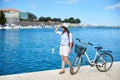 Happy attractive girl in sunglasses and with backpack riding a bike along stony sidewalk Royalty Free Stock Photo