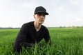 Happy attractive man in a black vintage shirt in a fashionable baseball cap sits in the green grass in a field. Royalty Free Stock Photo