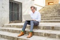 Happy attractive mature man working on laptop checking email sitting on stairs outdoors urban area Royalty Free Stock Photo