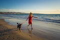 Happy attractive mature woman with her pet walking on friendly dog beach at sunset Royalty Free Stock Photo