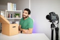 Happy attractive millennial arab guy with beard at workplace with camera and cardboard box