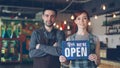 Happy attractive people cafe workers in aprons are holding Yes We Are Open sign and smiling while standing inside coffee Royalty Free Stock Photo