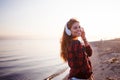 Happy attractive red-haired girl is enjoying music on walk. Beautiful young woman in shirt uses headphones, soft focus Royalty Free Stock Photo