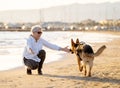 Happy attractive senior woman with her german shepard dog playing on the beach at autumn sunset Royalty Free Stock Photo