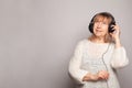 Happy attractive senior woman smiling relaxing listening to music with headphones and looking up on white studio wall background Royalty Free Stock Photo