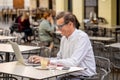 Happy attractive stylish mature man working on laptop while having coffee in outside coffee shop Royalty Free Stock Photo