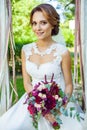 happy attractive wife holding wedding bouquet and sitting on swing at summer garden