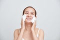 Happy attractive young Asian woman applying foaming cleanser on her face over white background