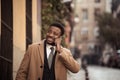 Happy attractive young business man on his smart phone while walking in the city smiling Royalty Free Stock Photo