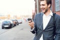 Happy attractive young businessman walking and using mobile phone outdoors. Royalty Free Stock Photo