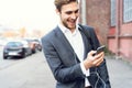 Happy attractive young businessman walking and using mobile phone outdoors. Royalty Free Stock Photo