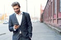 Happy attractive young businessman walking and using mobile phone outdoors. Royalty Free Stock Photo