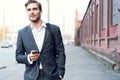 Happy attractive young businessman walking and using mobile phone outdoors. Royalty Free Stock Photo