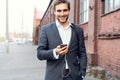 Happy attractive young businessman walking and using mobile phone outdoors. Royalty Free Stock Photo