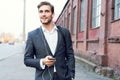 Happy attractive young businessman walking and using mobile phone outdoors. Royalty Free Stock Photo