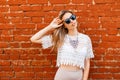 Happy attractive young hipster woman in sunglasses in a white lace blouse with a beautiful shiny necklace in a skirt posing near a Royalty Free Stock Photo