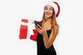 Happy attractive young woman in red christmas hat holding gift box and using mobile phone isolated on white background Royalty Free Stock Photo