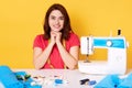 Happy attractive young woman seamstress sitting at working table, keeps hads under chin, looks happily at camera, beind in good Royalty Free Stock Photo