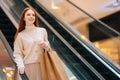 Happy attractive young woman shopaholic holding on escalator handrail and riding escalator going down in shopping mall Royalty Free Stock Photo