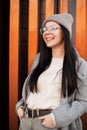 Happy attractive young woman with smile in fashionable knitted hat in stylish coat in fashion glasses poses outdoors in the city Royalty Free Stock Photo