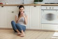 Happy attractive young woman using smartphone sitting on kitchen floor. Royalty Free Stock Photo