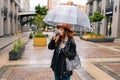 Happy attractive young woman wearing fashion hat standing with transparent umbrella in city cold rain and drinking hot Royalty Free Stock Photo