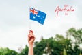 Happy Australia Day card with greeting text. Closeup of woman human hand arm waving Australian flag against blue sky. Proud Royalty Free Stock Photo