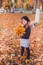 Happy autumn. A little girl in a red beret is playing with falling leaves and laughing.