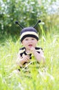 Happy baby in bee costume tastes grass on the meadow