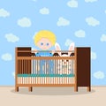 Happy baby boy in blue sleepwear standing in the wooden crib with soft toy