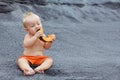 Happy baby boy eating orange papaya fruit on black beach