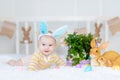 Happy baby boy with rabbit ears on his head lying with a rabbit on the bed with Easter eggs, cute funny smiling little baby. The Royalty Free Stock Photo