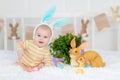 Happy baby boy with rabbit ears on his head lying with a rabbit on the bed with Easter eggs, cute funny smiling little baby. The Royalty Free Stock Photo