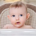 Happy baby with food stained mouth sitting on child chair, home kitchen background Royalty Free Stock Photo