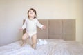 Happy baby girl has fun jumping and playing in big parent& x27;s bed with teddy bear. Funny child in parents bedroom having Royalty Free Stock Photo