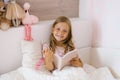 Happy baby girl with long hair reading a book on a bed with pillows Royalty Free Stock Photo