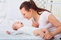 Happy baby girl lying near her mother on a white bed. Girls look Royalty Free Stock Photo